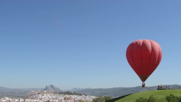 Red Hot Air Balloon Taking Off with Antequera Village at Background alt
