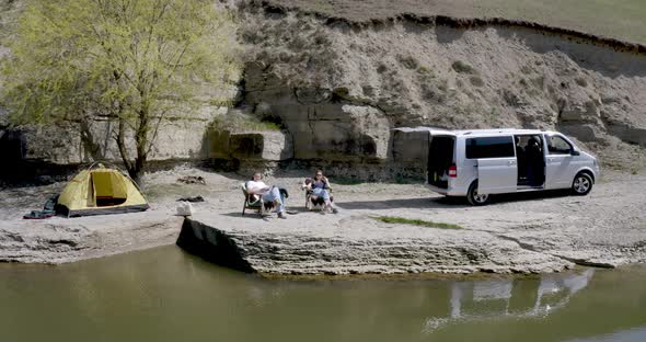 drone view of a guy and a girl sitting on armchairs in a campsite on the lake near the motor home alt