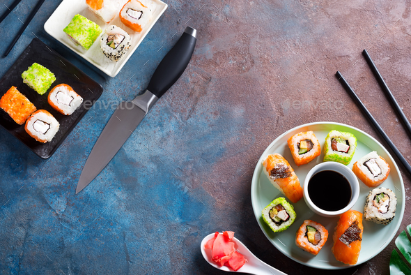 Freshly cooked sushi and rolls set with soy sauce on a ceramic plate with knife, metal chopsticks on