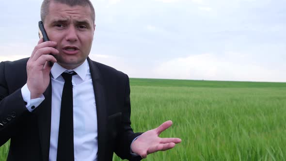 Angry Businessman Talking on a Smartphone in the Middle of the Field alt