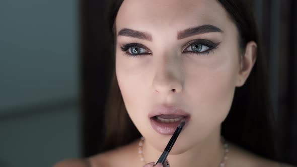 Woman with Bright Makeup Applies Lipstick to Her Plump Lips alt