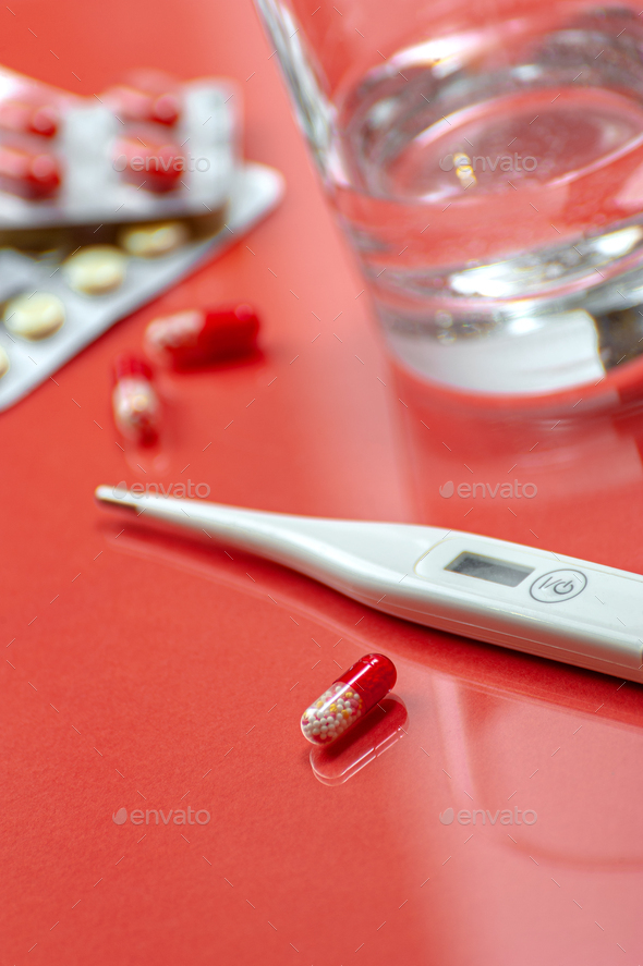 Antibiotics, a glass of water and a thermometer on a red background. Photo shallow depth of field. - Stock Photo - Images