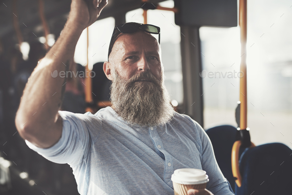 Mature bearded man standing on a bus drinking coffee