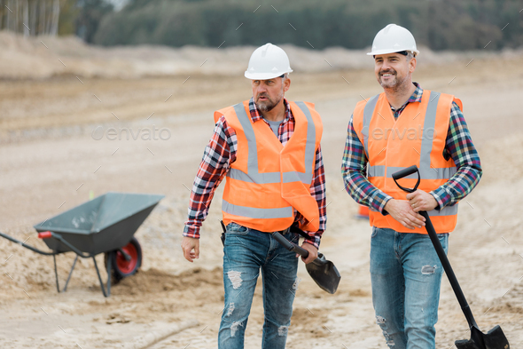 Two builders in orange vests and helmets working on the road construction field