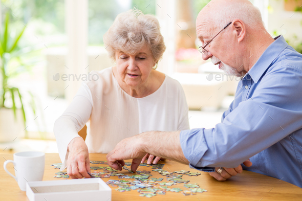 Cute grandma and grandpa put puzzle pieces together at home