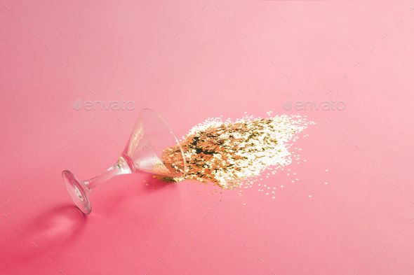 Spilled martini glass full of gold glitter on pink background. Creative