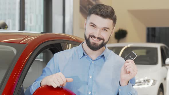 Happy Attractive Man Showing Car Keys to the Camera at Dealership Salon alt