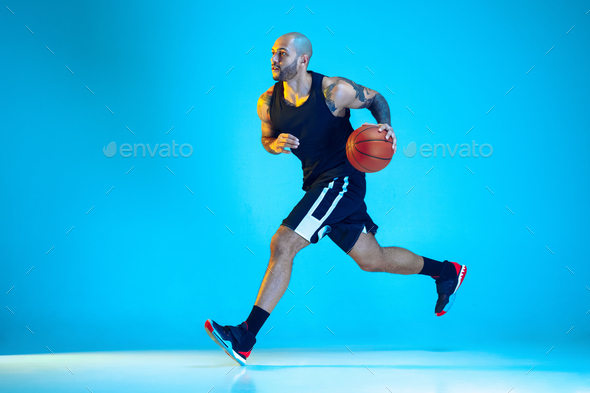 Young basketball player training isolated on blue studio background in neon light