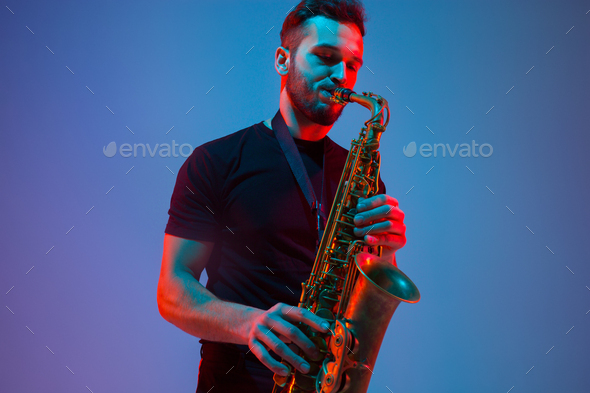 Young caucasian jazz musician playing the saxophone in neon light