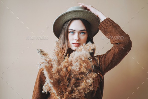 Young beautiful long hair girl in felt hat and brown knitted sweater with dried flowers in hands