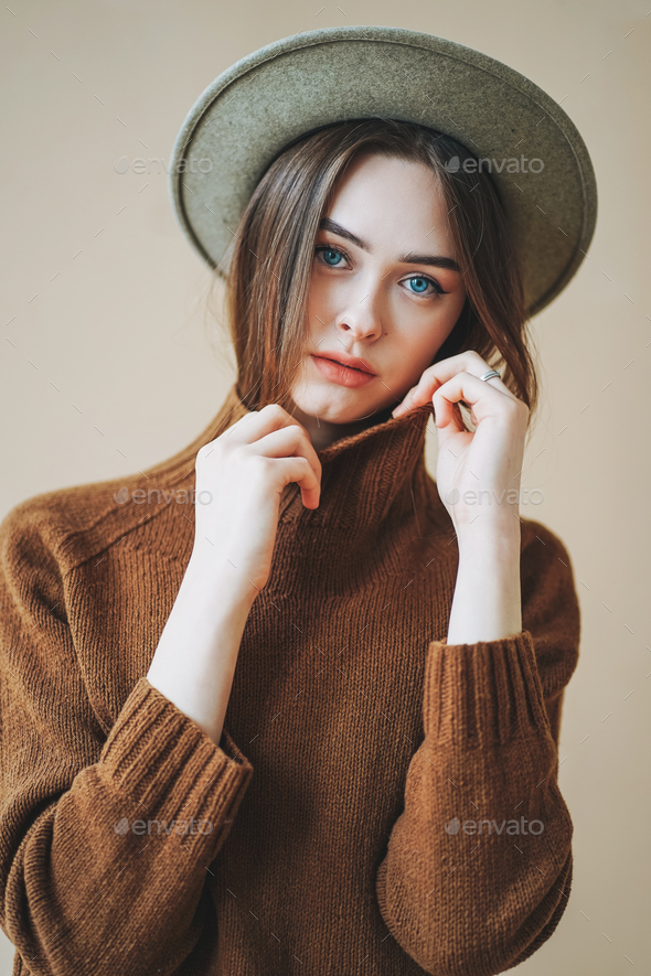 Young beautiful long brown-haired hair girl with blue eyes in felt hat and brown knitted sweater