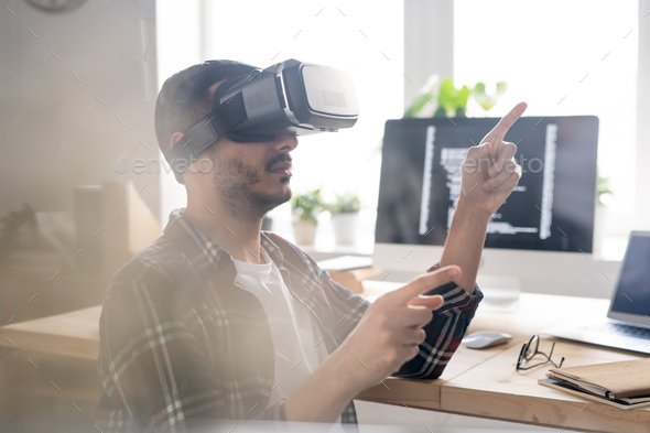 Contemporary software developer in vr headset pointing at virtual display