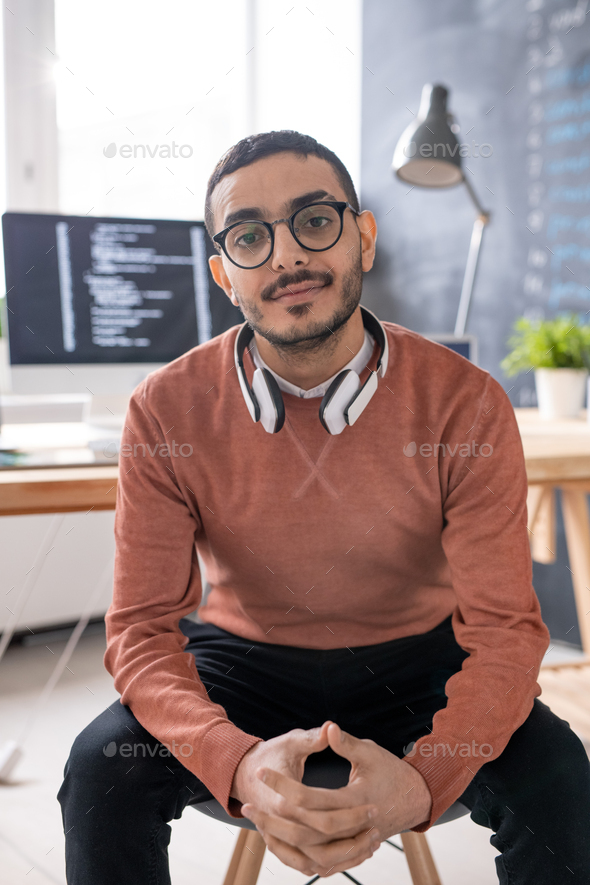 Young programmer with headphones looking at you while sitting in front of camera