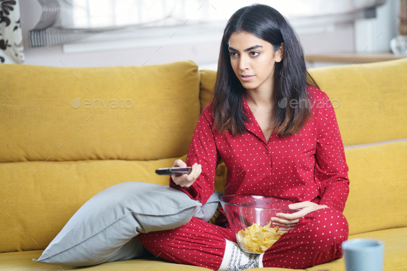 Persian woman at home watching TV and using remote control