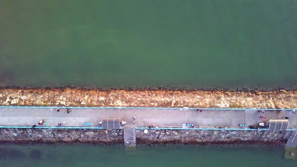 A dynamic top-down aerial shot of a breakwater jetty made out of stones with a paved pathway for civ alt