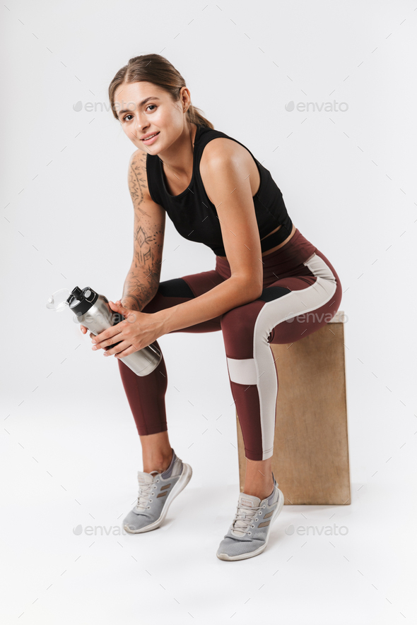 Pleased sports woman isolated over white wall background have a rest drinking water.