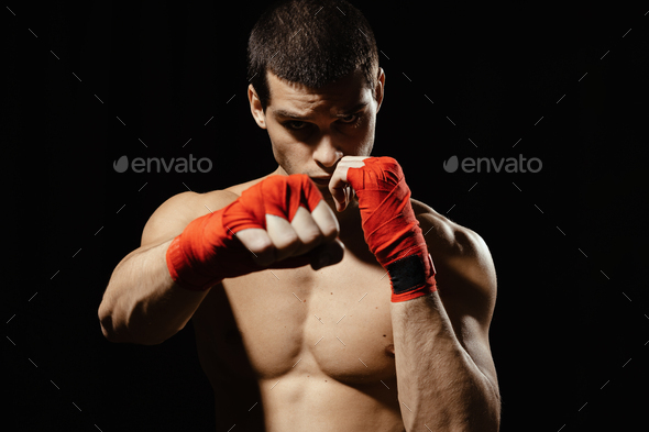 Athletic boxer punching with determination and precaution over black background