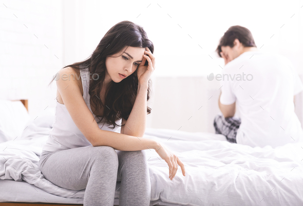 Sad married couple sitting on bed after quarrel