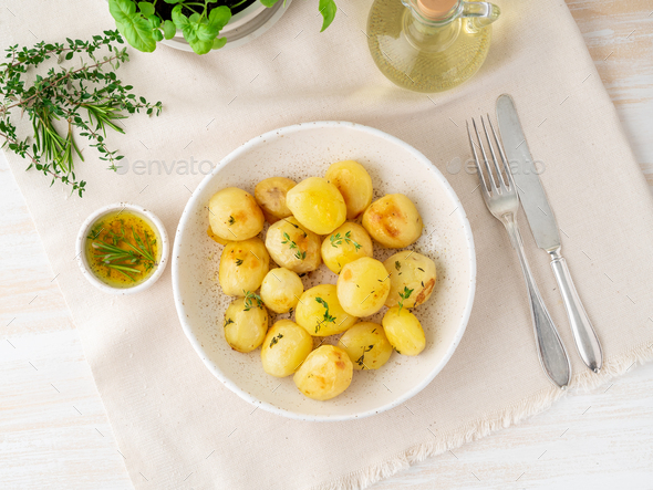 baked in oven with spices round whole potato tubers in plate on white textile background