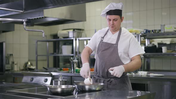 Concentrated Caucasian Professional Cook Pouring Vegetable Oil in Cooking Pan in Slow Motion Setting alt