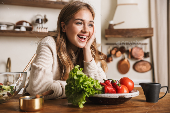 Image of joyful caucasian woman laughing while cooking dinner