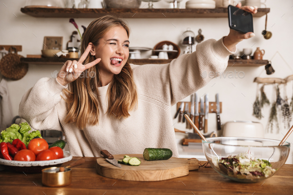 Image of funny cute woman taking selfie on cellphone and gesturing peace sign