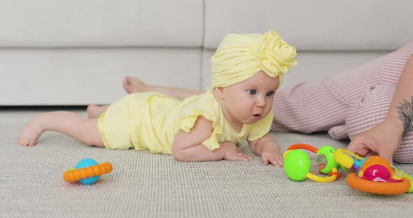A Nice Little Caucasian Newborn Baby Girl in a Yellow Outfit and in a Turban is Lying on the Floor
