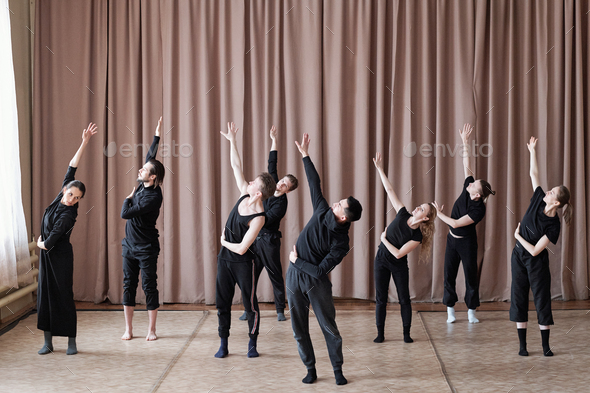 Five guys and three girls in black activewear stretching one arm upwards