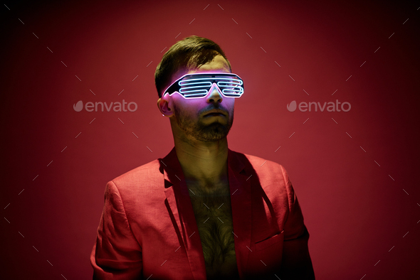Contemporary young man in red jacket and high tech eyewear standing in darkness
