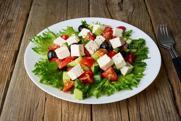 Greek salad on white plate on old rustic wooden table, side view