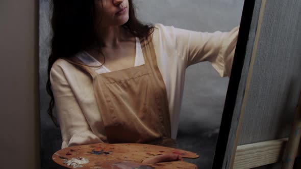 Young Woman Artist Mixing Colors on the Palette with a Brush and Applying in on the Canvas alt