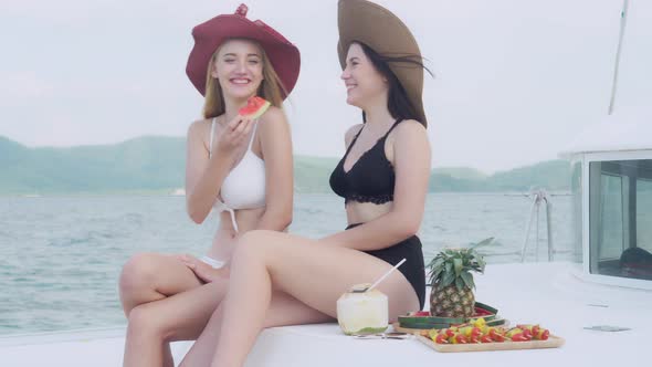 Two young woman in bikini sexy to travel sitting and eating watermelon in party for leisure. alt