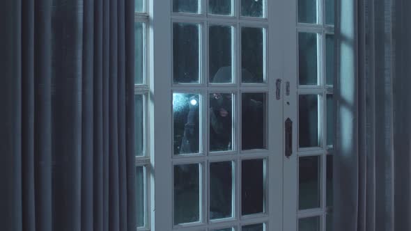 Thief Man Holding Flashlight Looking Inside The House While Standing Outside In The Dark Night alt