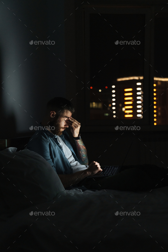 young bearded man laying on bed at home at night