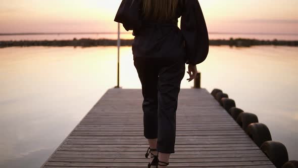 Tracking Backside Footage of a Tall Long Haired Woman Walking in Black Clothes By the Pier alt