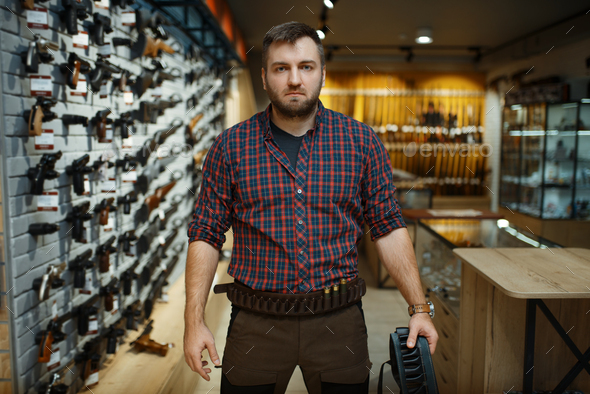 Man in hunting uniform holds ammo belt in gun shop