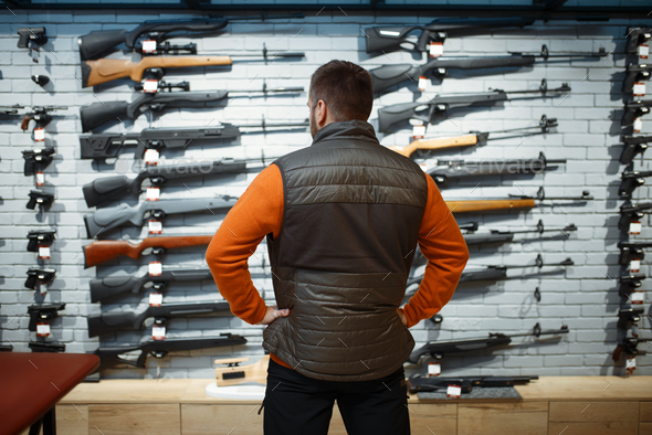 Man at showcase with rifles, back view, gun shop