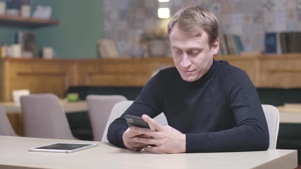 Concentrated Man Using Smartphone Sitting in Restaurant As Cute Cheerful Girl Coming Taking Device alt