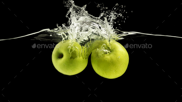 Two green apples splattering into water with waves on black background, panorama