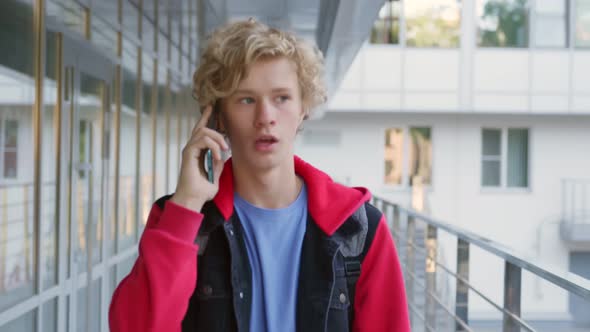 Slider Shot of Happy Schoolboy Walking on Street to School and Talking on Cellphone alt