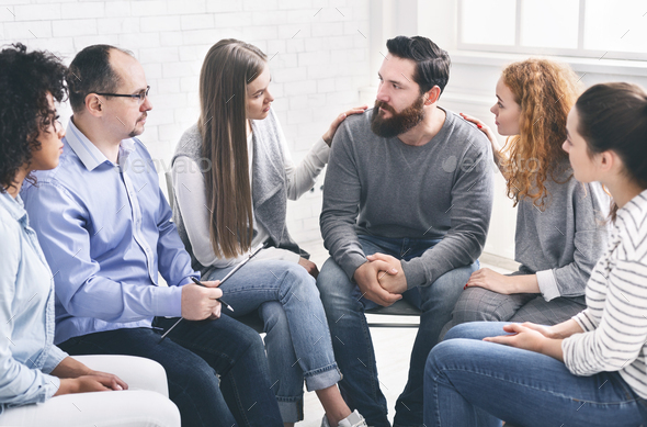 Therapy Group Members Comforting Upset Man On Community Meeting In Rehab
