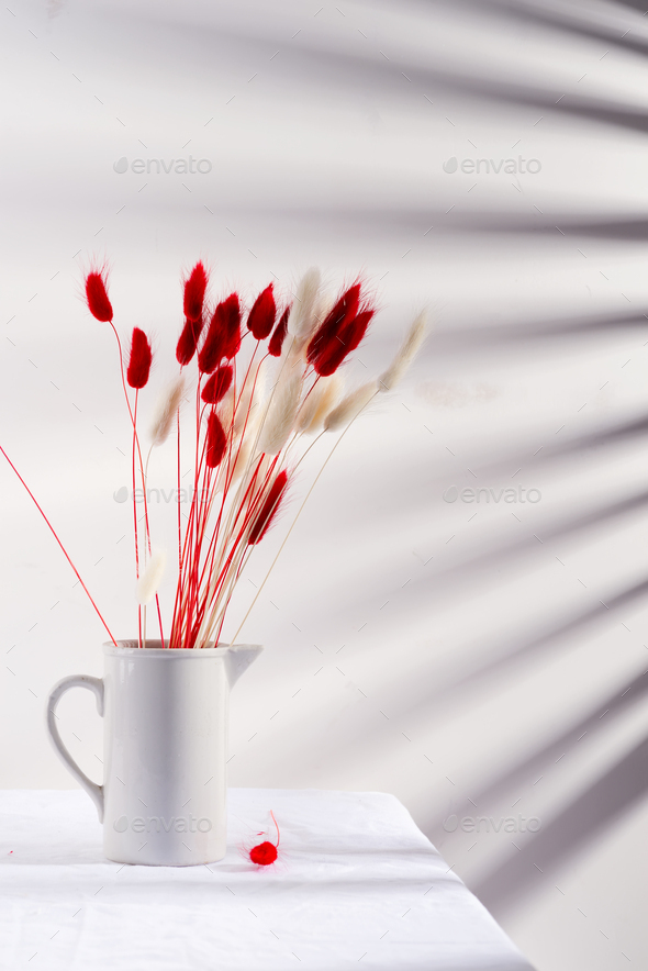Ceramic mug with dry soft autumn red and white flowers Lagurus Ovatus grass on a table covered