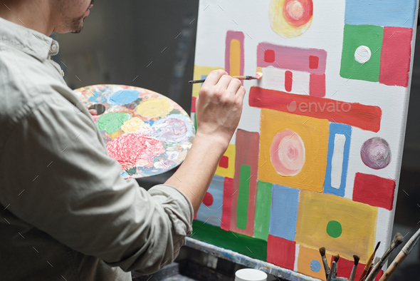 Young male artist with color palette and paintbrush working over painting - Stock Photo - Images