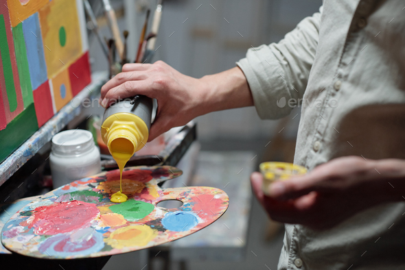 Hand of young painter adding yellow color on palette before start painting - Stock Photo - Images