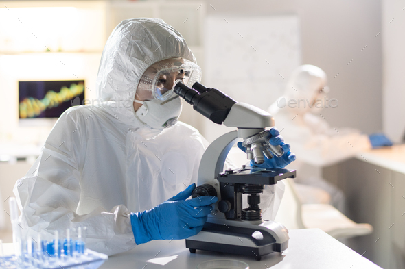 Female lab worker or researcher looking at new chemical element in microscope