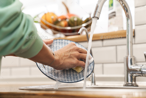 Woman indoors at home wash the dishes at the kitchen.