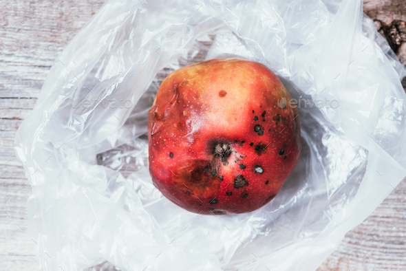 Spoiled bad red apple on plastic bag background. Garbage dump rotten food. Top view. Copy space