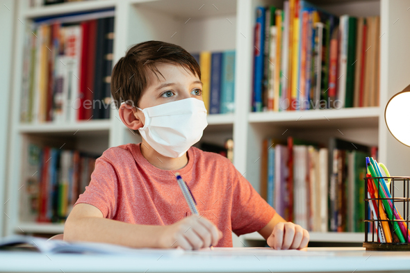 Young student wearing protective mask working in isolation on school assignments.