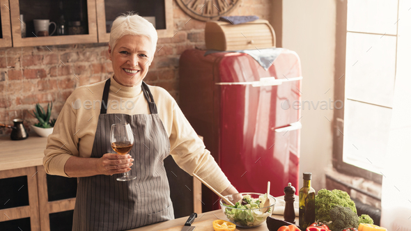 Positive Elderly Woman With Wine Glass In Hands Posing In Kitchen
