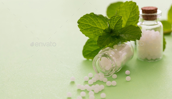 Homeopathy, globules scattered out of glass bottle, green background Stock  Photo by rawf8